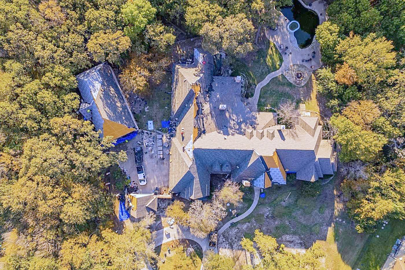 Overhead drone view of a reroof in progress with tarps among autumn trees